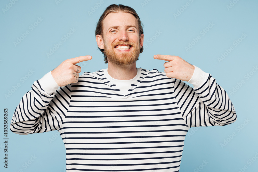Young smiling happy man he wear striped sweatshirt casual clothes point index finger on opened mouth white teeth isolated on plain pastel light blue cyan background studio portrait. Lifestyle concept. Young smiling happy man he wear striped sweatshirt casual clothes point index finger on opened mouth white teeth isolated on plain pastel light blue cyan background studio portrait. Lifestyle concept.