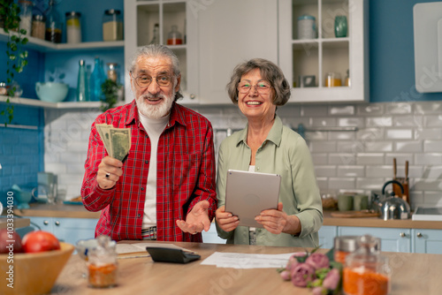 in a bright kitchen an elderly cute couple at the table count their expenses monthly payment utility bills count money smiling checking on tablet laughing