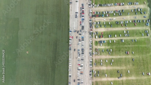 This aerial image shows a large agricultural event or trade fair, amidst expansive fields. Multiple rows of tents, machinery, and equipment are neatly arranged on a long track, attracting numerous