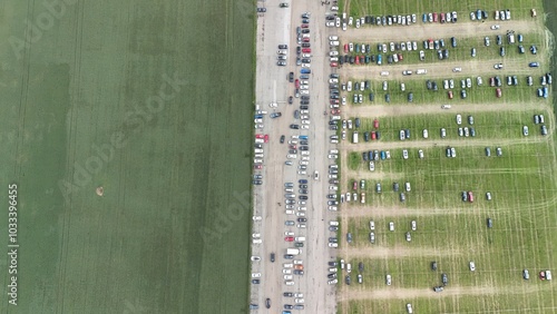 This aerial image shows a large agricultural event or trade fair, amidst expansive fields. Multiple rows of tents, machinery, and equipment are neatly arranged on a long track, attracting numerous