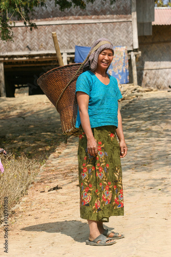 Bangladeshi rural tribal lady walking on a road with a traditional bucket on her back photo