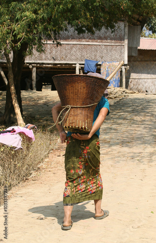 Bangladeshi rural tribal lady walking on a road with a traditional bucket on her back photo