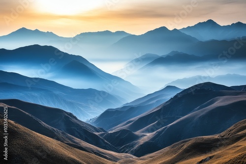 A stunning panorama of layered mountain ranges bathed in the soft light of sunrise or sunset, with a veil of mist clinging to the slopes.