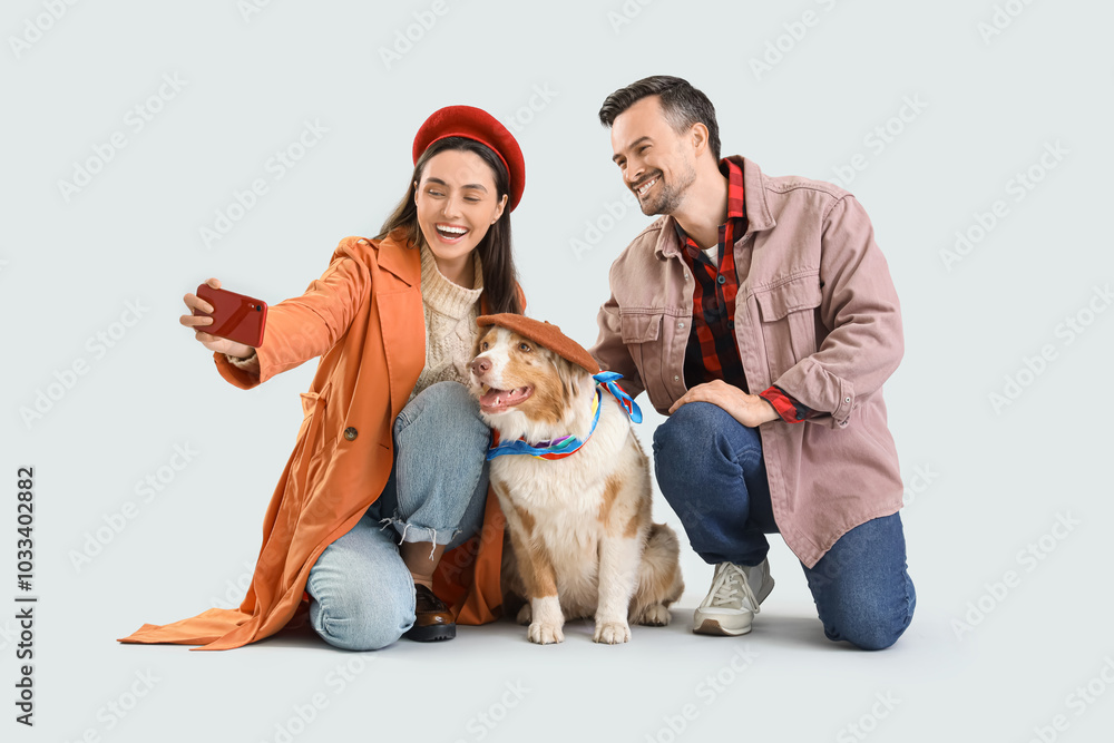 Young couple in autumn clothes with Australian Shepherd dog taking selfie on light background Young couple in autumn clothes with Australian Shepherd dog taking selfie on light background