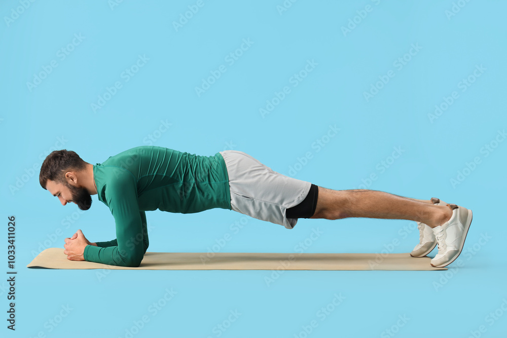 Naklejka premium Sporty young man exercising on yoga mat against blue background