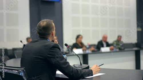 Press conference at round table. Speaker man CEO press conference forum seminar. Group of multiracial colleagues listening. Closeup of hands. Businessman speaking microphone discussion board meeting.
