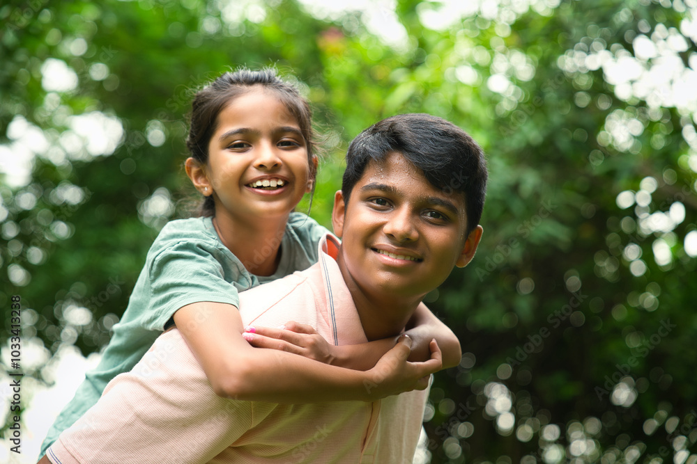 Indian big brother giving playful piggyback ride to his little sister outdoors in nature Indian big brother giving playful piggyback ride to his little sister outdoors in nature
