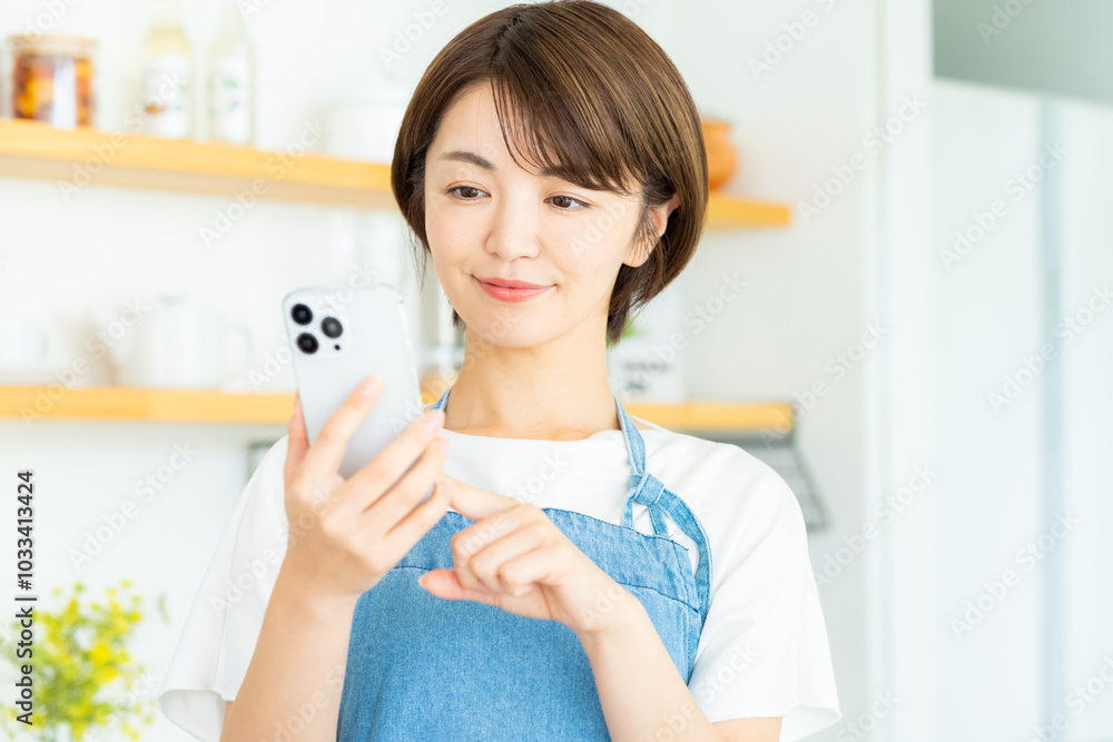 キッチンでスマホを持つ笑顔の女性 キッチンでスマホを持つ笑顔の女性