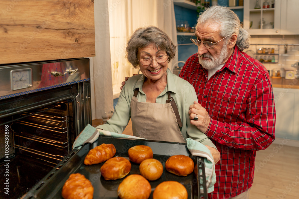 in bright kitchen an elderly woman in a light green shirt takes fresh pies out of the oven happy old age housewife in the kitchen husband hugs from behind in bright kitchen an elderly woman in a light green shirt takes fresh pies out of the oven happy old age housewife in the kitchen husband hugs from behind