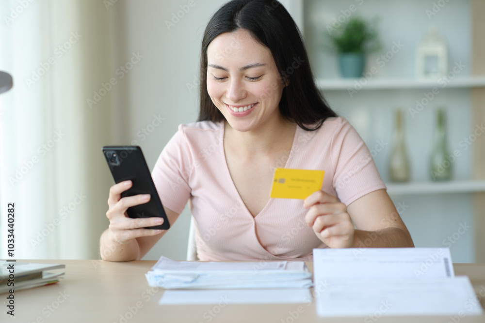 Happy asian woman paying bills with phone and card at home Happy asian woman paying bills with phone and card at home