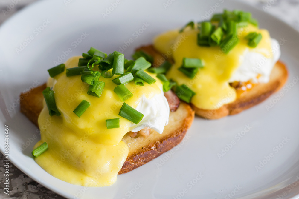 Delicious English breakfast. Eggs benedict with sauce and bacon on toasted white bread on a gray plate, close-up on a light background