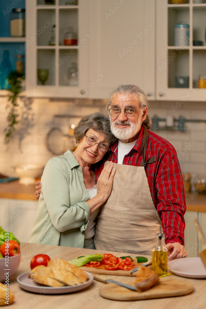 close up in bright kitchen an elderly woman in a light green shirt with her husband in an apron are standing in the kitchen hugging, smiling, looking at the camera close up in bright kitchen an elderly woman in a light green shirt with her husband in an apron are standing in the kitchen hugging, smiling, looking at the camera