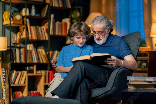 a warm light of living room with library big blue armchair grandfather sitting with grandson reading fairy tale hugging grandson