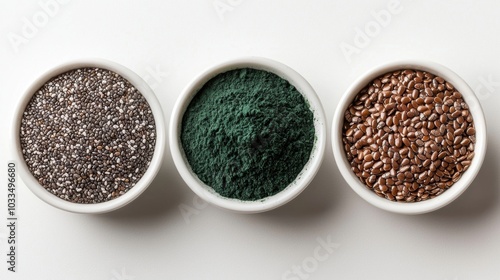 Three bowls of different seeds: black chia green spirulina powder and brown flaxseed displayed on a light background