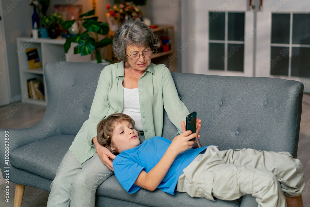 bright living room with sofa grandmother sitting on sofa grandson lying and watching cartoons on tablet happy family bright living room with sofa grandmother sitting on sofa grandson lying and watching cartoons on tablet happy family