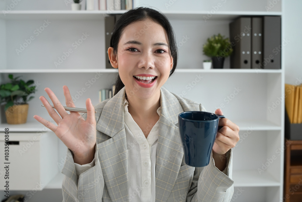Smiling young businesswoman with coffee cup in hand talking during video call in the office