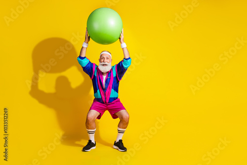 Full length photo of handsome good mood senior guy oldschool sportswear rising fit ball emtpy space isolated yellow color background photo