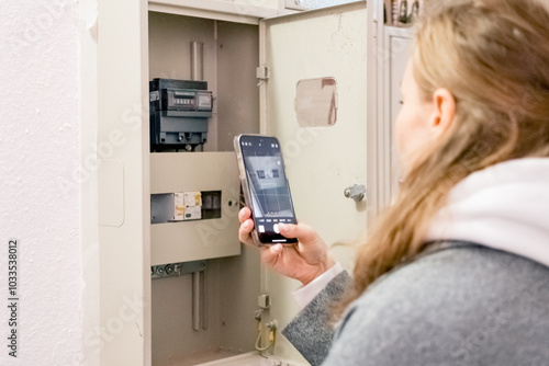A young woman takes readings from an electric meter for further payment.