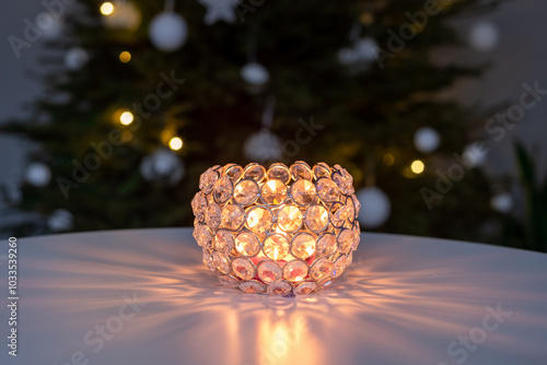 Crystal tealight candle holder casting warm light with christmas tree in background, Christmas background with copy space