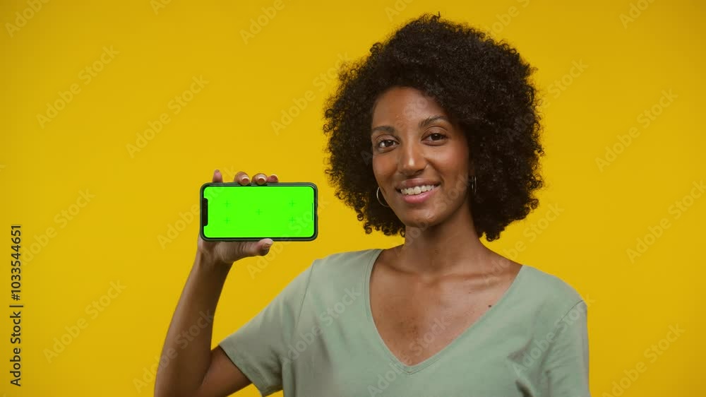 Smiling Woman Holding Smartphone with Green Screen on Yellow Background