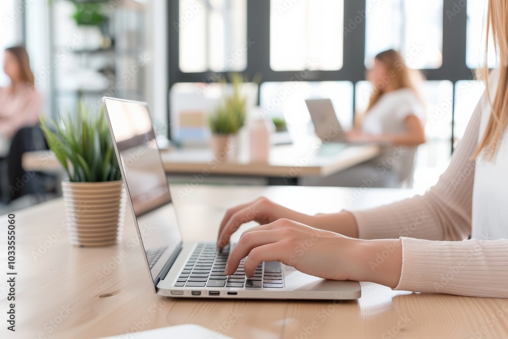 A woman typing on a laptop in a modern, bright co-working space with other people working in the background. A woman typing on a laptop in a modern, bright co-working space with other people working in the background.