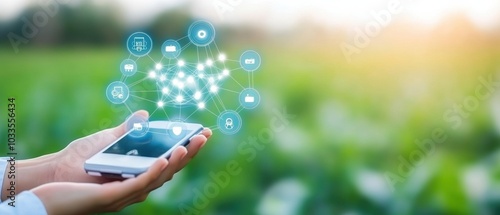 A hand holding a smartphone with digital icons over a green field, representing connectivity and technology in agriculture.