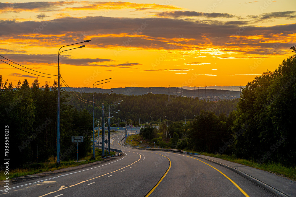 Fototapeta premium photo of road going into sunset, beautiful orange bright sunset sky, road winding along forest, electric poles, marking, trees and forest, road romance
