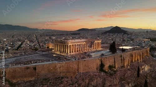 Flying around Parthenon in Athens, Greece at sunrise. Acropolis with city lights and Athens city below. Top international landmark in Greece. Aerial shot, UHD