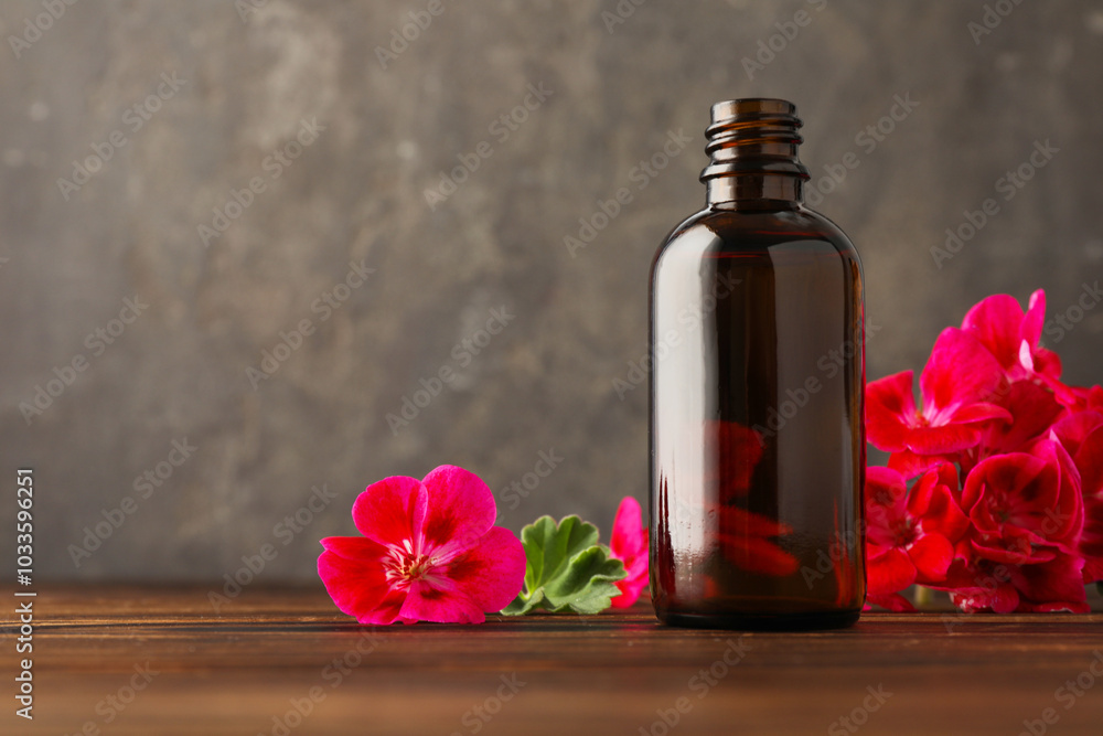 Geranium essential oil in bottle and beautiful flowers on wooden table Geranium essential oil in bottle and beautiful flowers on wooden table