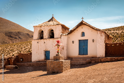 The lovely church of Machuca, a small village at 4000m of altitude near San Pedro de Atacama in Chile. The church features traditional adobe architecture including thatched roof and blue doors. photo