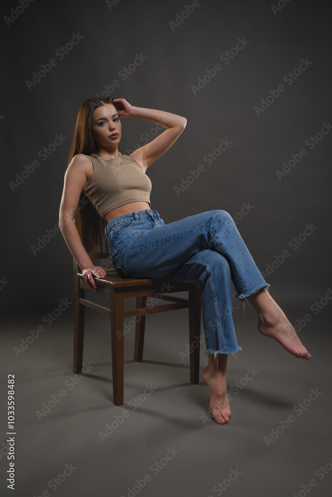Beautiful girl posing with a chair on a gray background. Beauty and fashion. Beautiful girl posing with a chair on a gray background. Beauty and fashion.