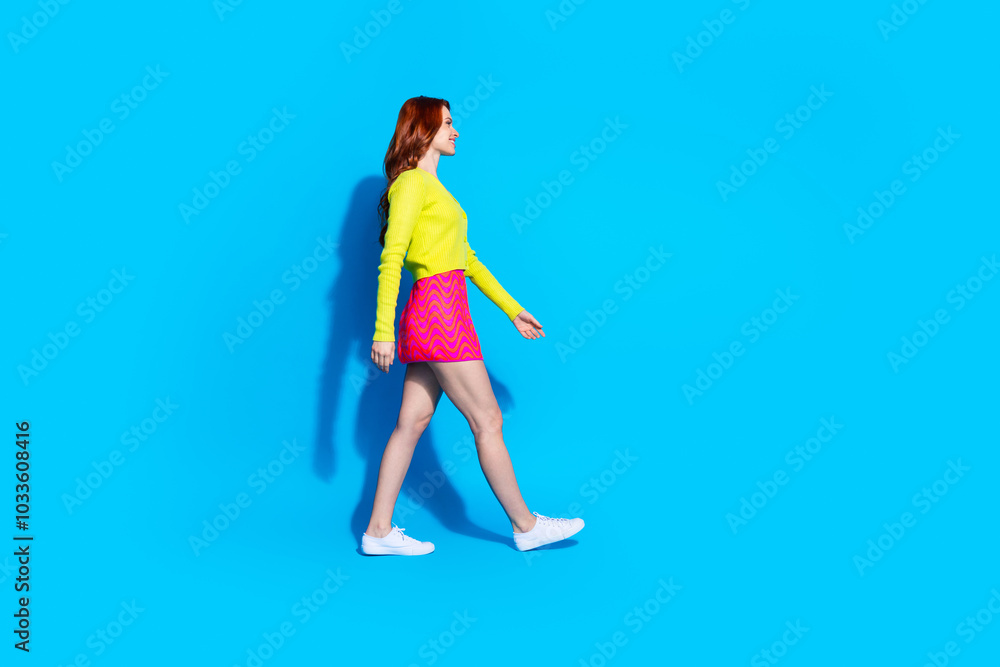 Full length photo of lovely young lady walking profile dressed stylish yellow garment isolated on blue color background Full length photo of lovely young lady walking profile dressed stylish yellow garment isolated on blue color background