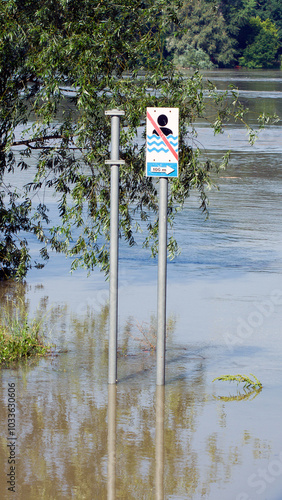 A striking image depicting a flooded area, with road signs partially submerged in water. The scene captures the severity of the flooding, with reflections shimmering on the surface and debris scattere
