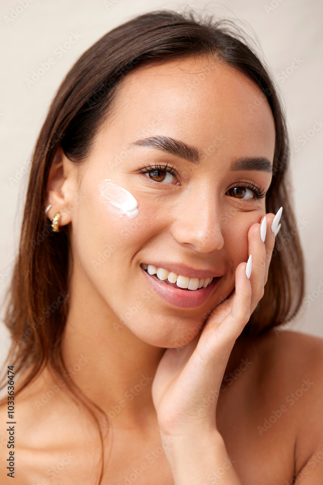 Young woman applying facial moisturizer, smiling at camera Young woman applying facial moisturizer, smiling at camera