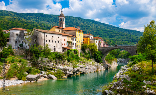 Panoramic view of slovenian village “Kanal ob Soči“ on a summer day. Picturesque scenery with old arch bridge, colorful houses and church on famous Isonzo (Soča) river with emerald turquoise water.