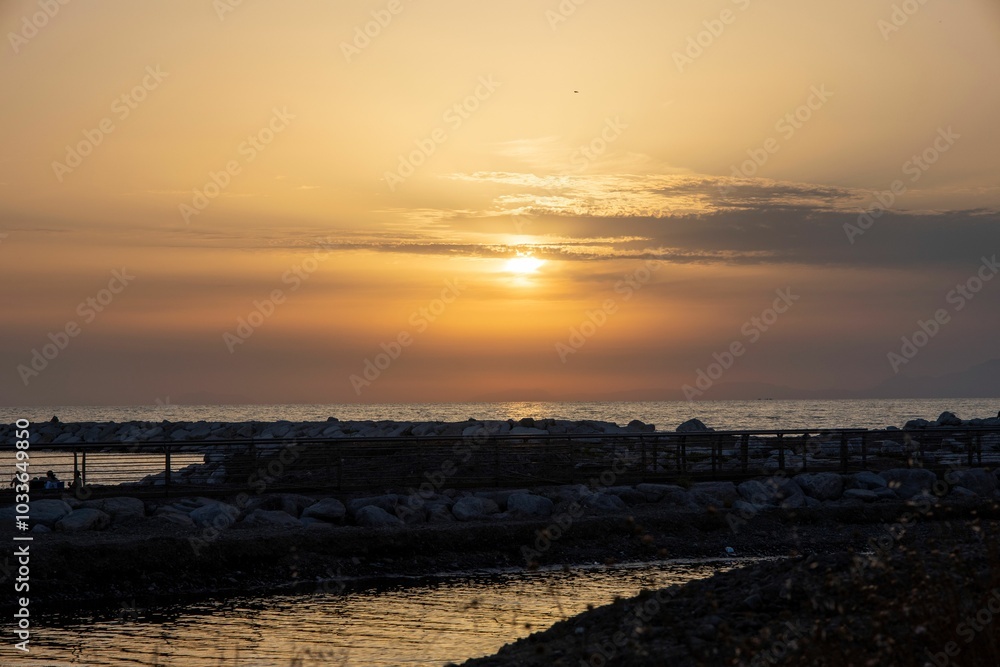 Scenic sunset over a rocky coastline with a calm sea and a clear sky. Scenic sunset over a rocky coastline with a calm sea and a clear sky.
