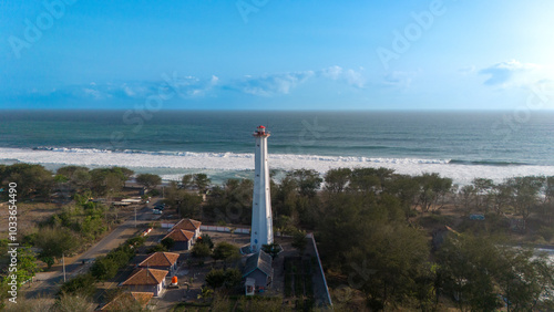 Wallpaper Mural A tall lighthouse stands by the shore with gentle ocean waves and lush greenery in the backdrop Torontodigital.ca