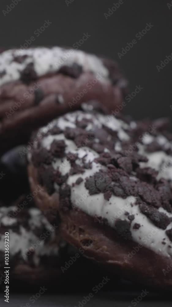 Close-up vertical shots of chocolate donuts with white topping against black background Close-up vertical shots of chocolate donuts with white topping against black background