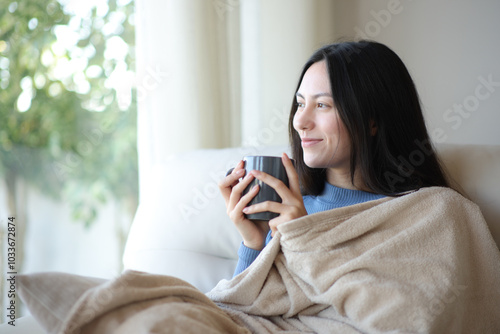 Relaxed asian woman looking through a window keeping warm