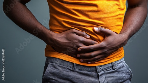 Person in casual wear with a hand on their stomach wincing in pain standing against a neutral backdrop Stock Photo with side copy space