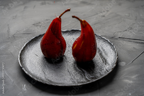 Pears stewed in red wine are poured with sauce on a black mica plate on a dark background.