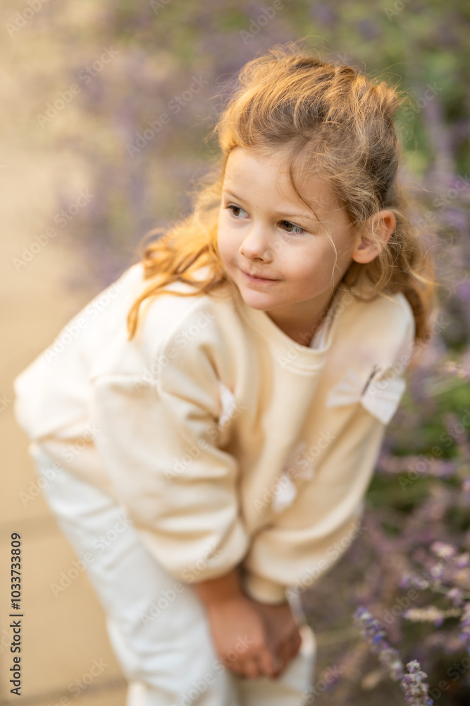 Little girl walking in the park in autumn and touching flowers in the garden. A cute girl in white clothes is standing in a flower alley. Little girl walking in the park in autumn and touching flowers in the garden. A cute girl in white clothes is standing in a flower alley.