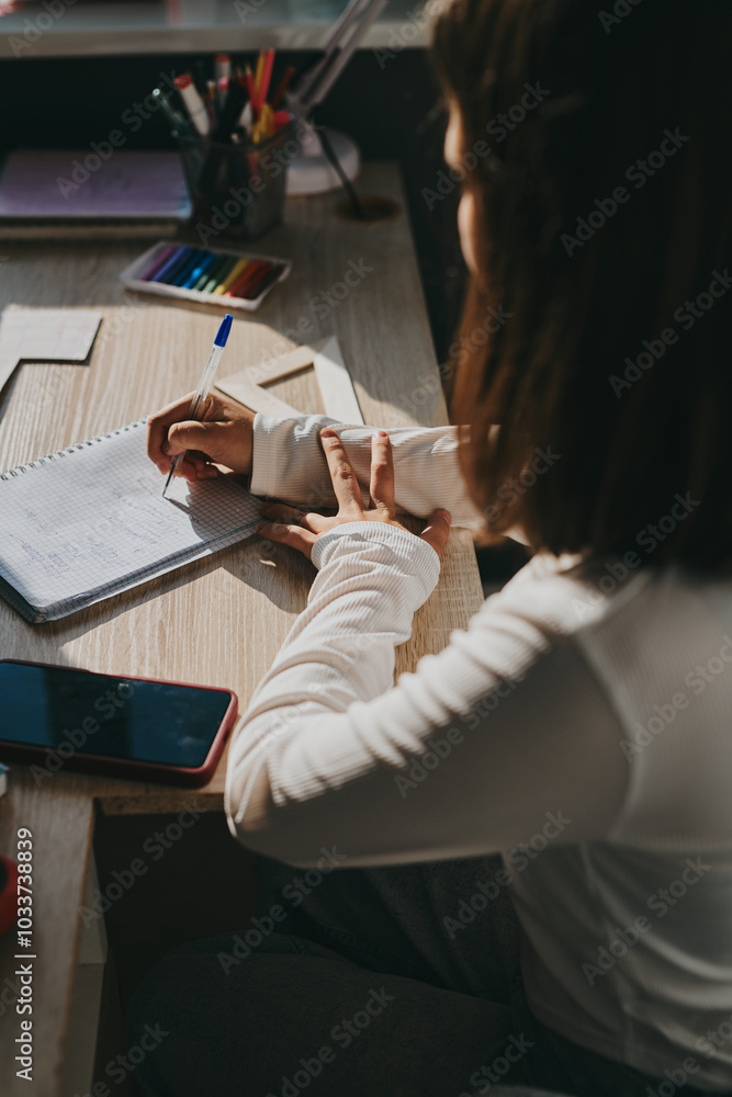 Obraz premium Schoolgirl at home schooling. The girl sits at the table with textbooks doing homework