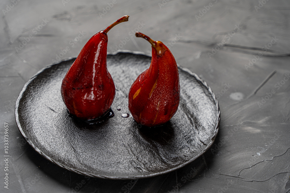 Pears stewed in red wine are poured with sauce on a black mica plate on a dark background. Pears stewed in red wine are poured with sauce on a black mica plate on a dark background.