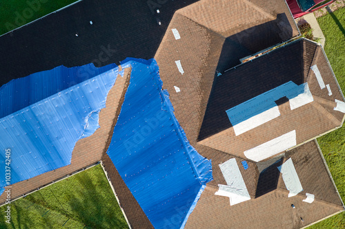 Aerial view of damaged in hurricane Ian house roof covered with blue protective tarp against rain water leaking until replacement of asphalt shingles photo