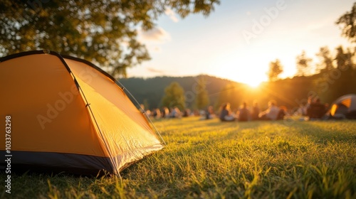 An orange tent is vibrantly lit by the golden sunlight while people gather and relax on the lush grass, enjoying a tranquil sunset in a picturesque outdoor venue. photo