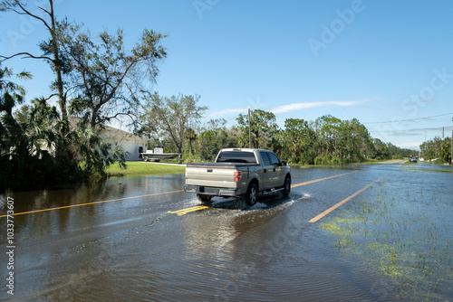 Flooded american street with moving vehicles and surrounded with water houses in Florida residential area. Consequences of hurricane natural disaster