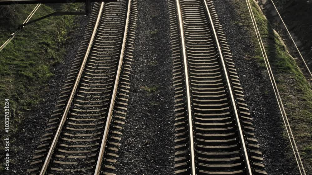 An elevated view shows two curved railway tracks surrounded by lush greenery during the golden hour An elevated view shows two curved railway tracks surrounded by lush greenery during the golden hour