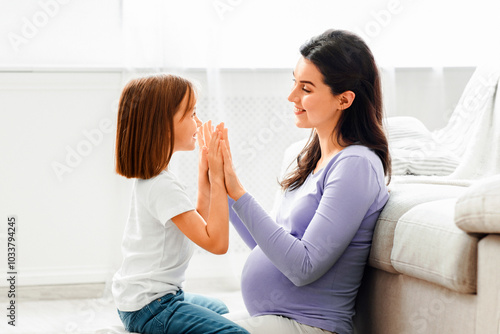 Pregnant young woman playing with her little daughter at home, sitting on floor, copy space