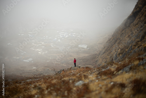 Obraz na plátne A person in a red jacket stands on a misty hillside overlooking a foggy valley
